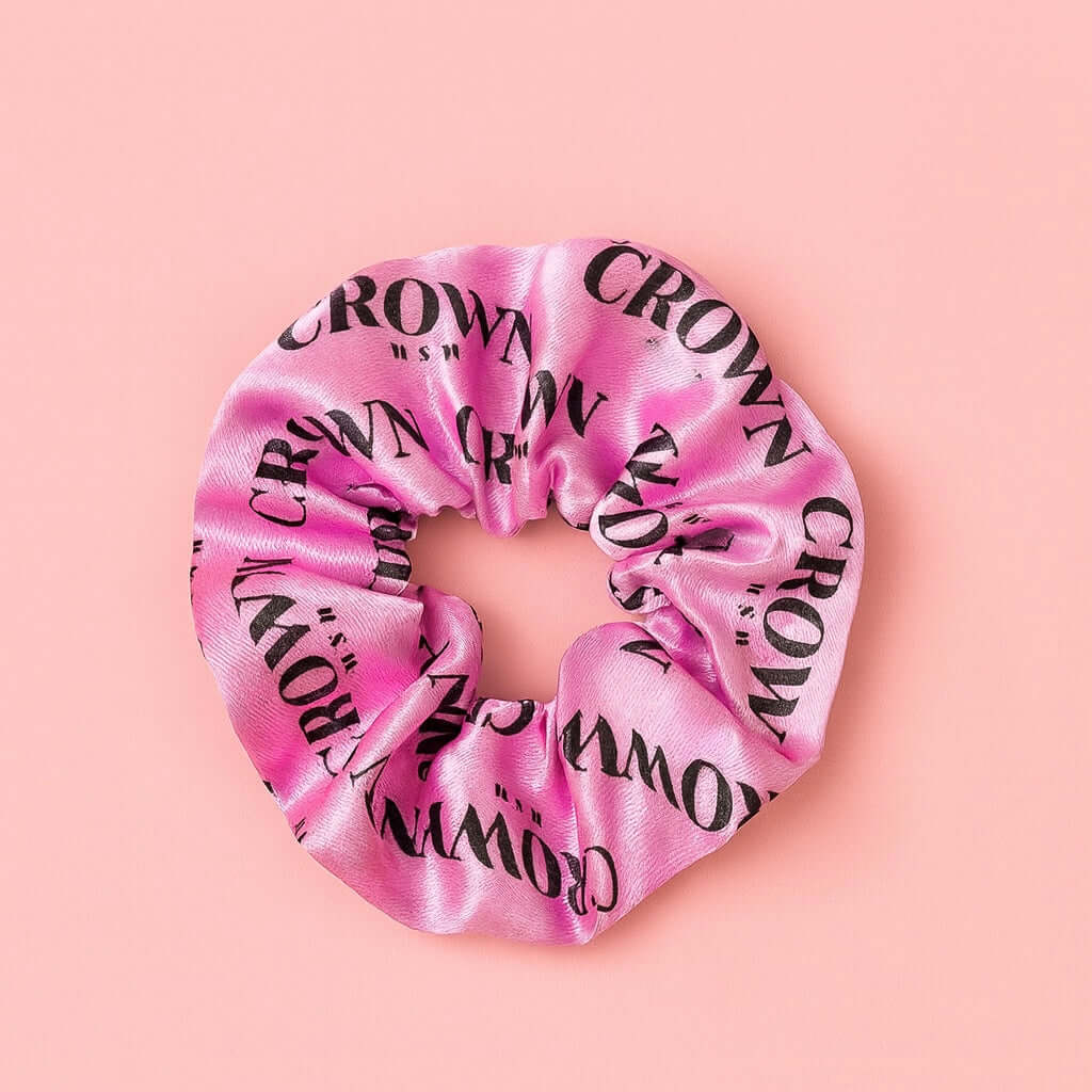 Satin Scrunchie in soft pink with CROWN WASH logo, perfect for styling hair and reducing frizz.